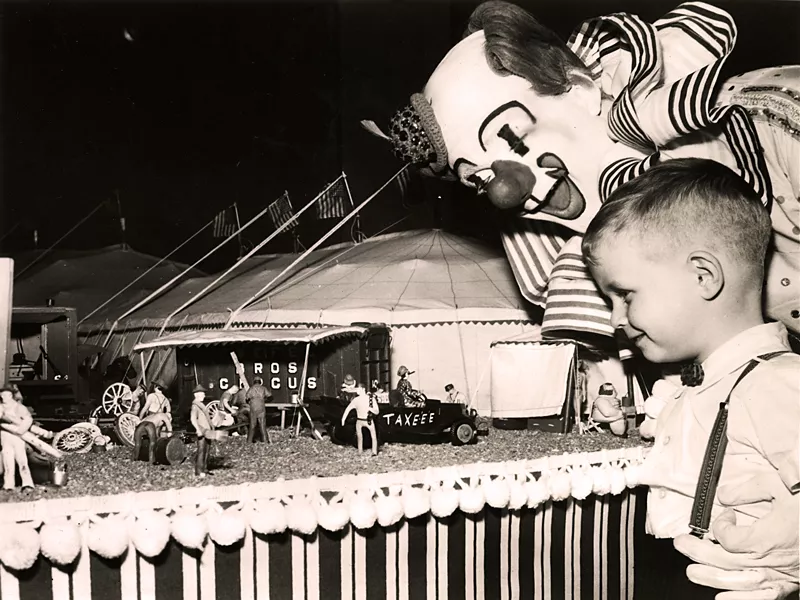 Small boy standing next to a clown looking at a model circus.