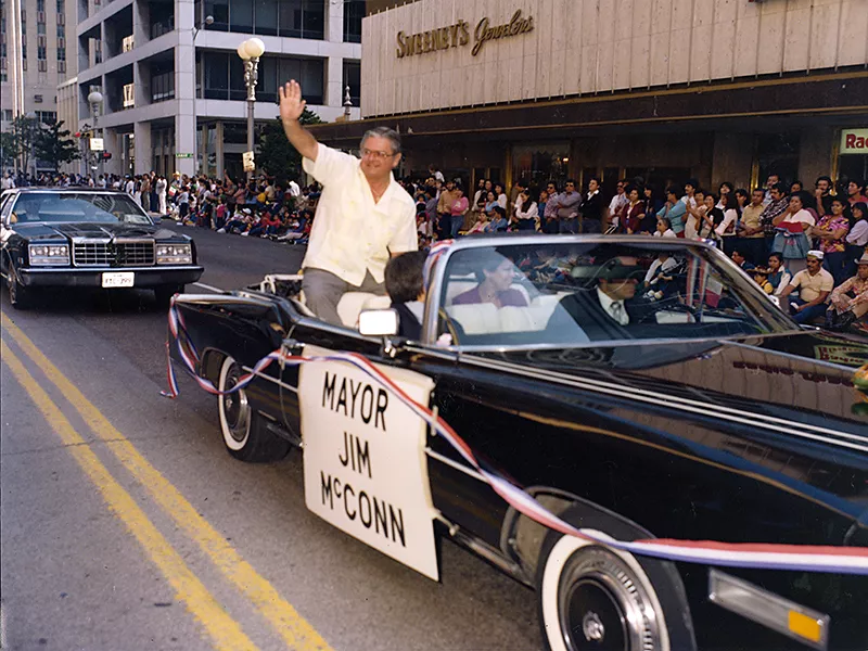Mayor Jim McConn riding a car in a parade, and waving to the crowd