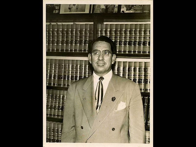 John J. Herrera in front of bookshelf