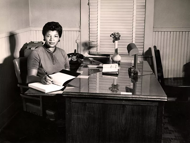 Sulena L. Gordon sitting behind a desk and writing in a notebook.