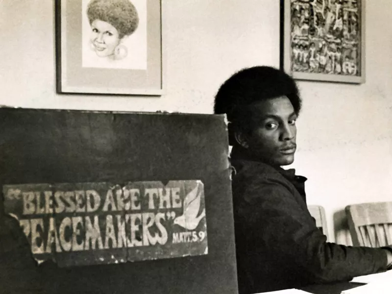 African American man sitting at a table next to a sign reading "Blessed are the Peacemakers."